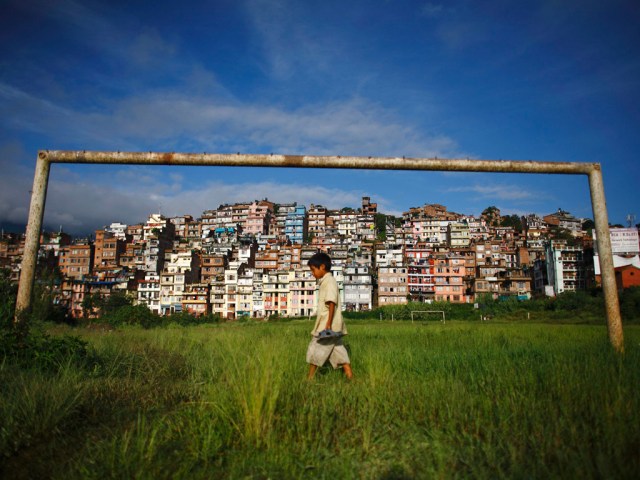 A boy walks past a football post near the ancient city of Kirtipur